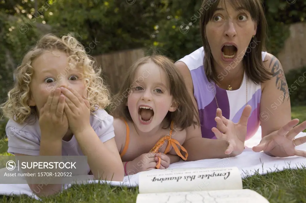 A woman and two girls screaming whilst lying down in a backyard
