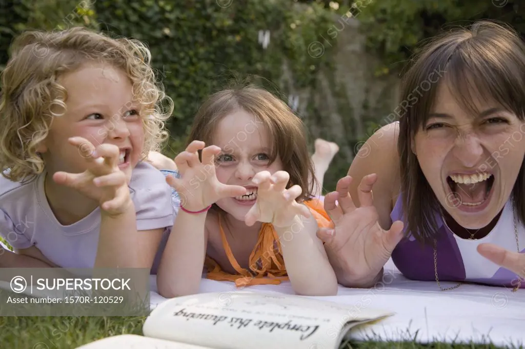 A woman and two girls growling whilst lying down in a backyard