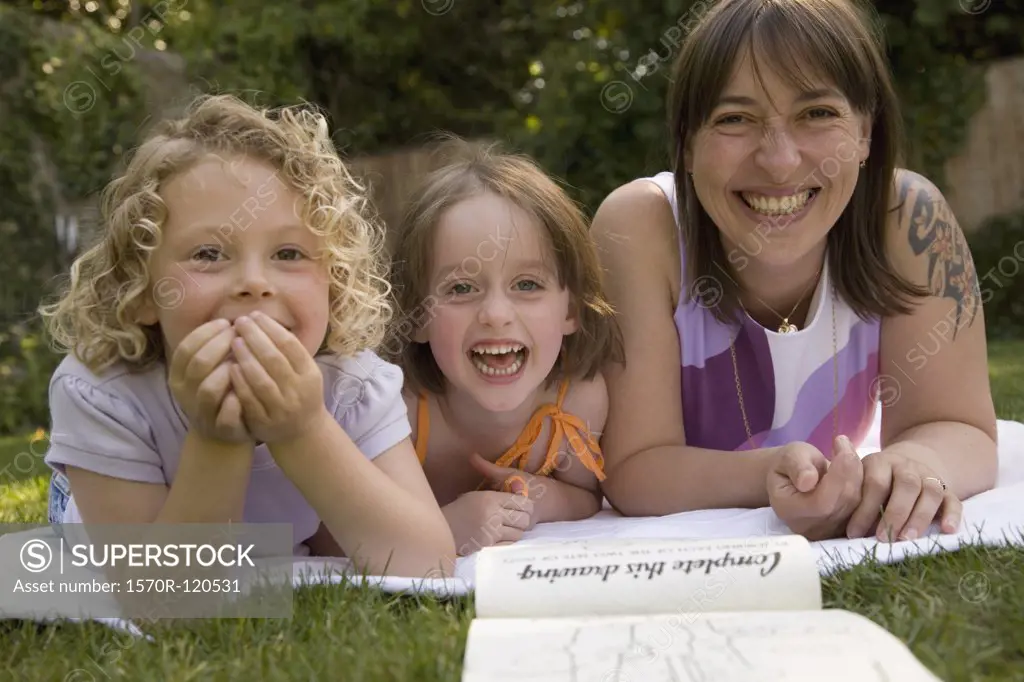 A woman and two girls laughing whilst lying down in a backyard