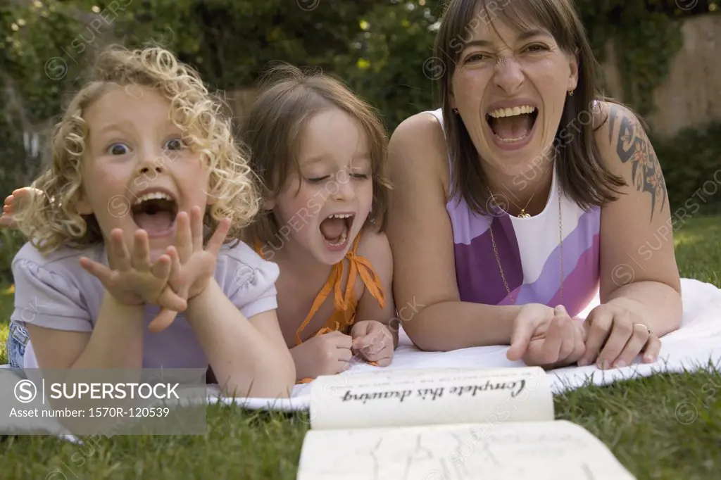 A woman and two girls laughing whilst lying down in a backyard