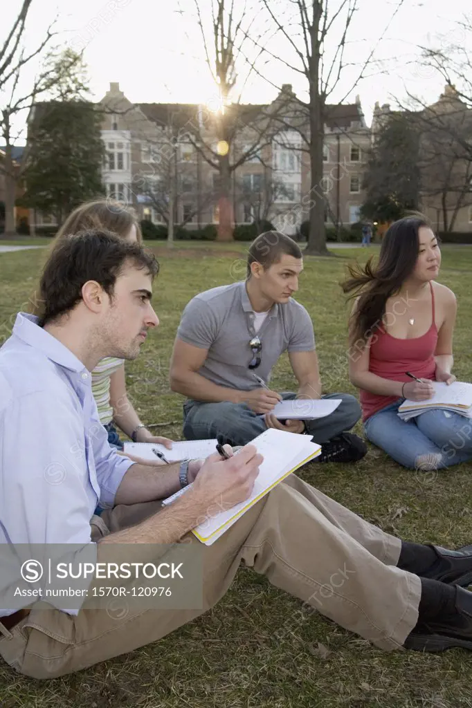 University students sitting on grass writing
