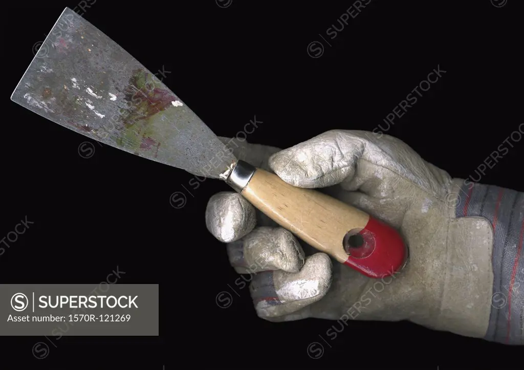 Person wearing a work glove and holding a putty knife