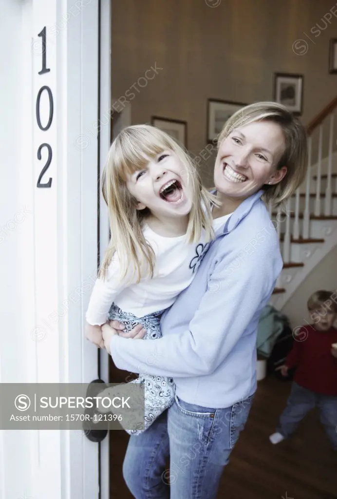 A mother holding her daughter in the front entrance of a suburban house