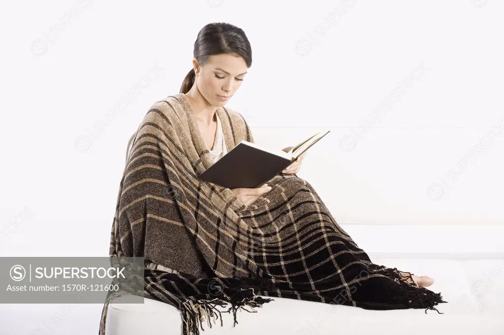A woman wrapped in a blanket and reading a book
