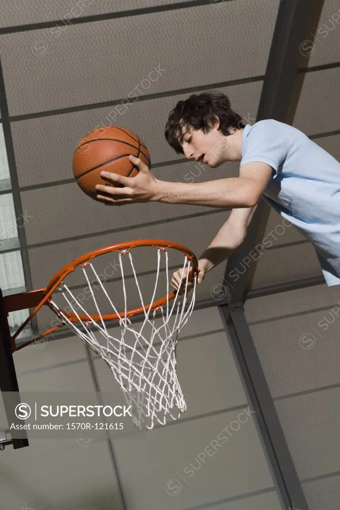 A young man standing above basketball hoop holding ball