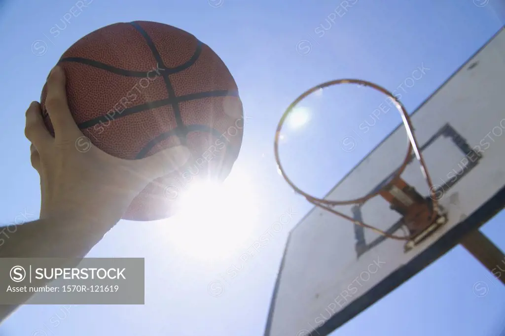 A human hand reaching up towards the sun and basketball hoop with holding basketball
