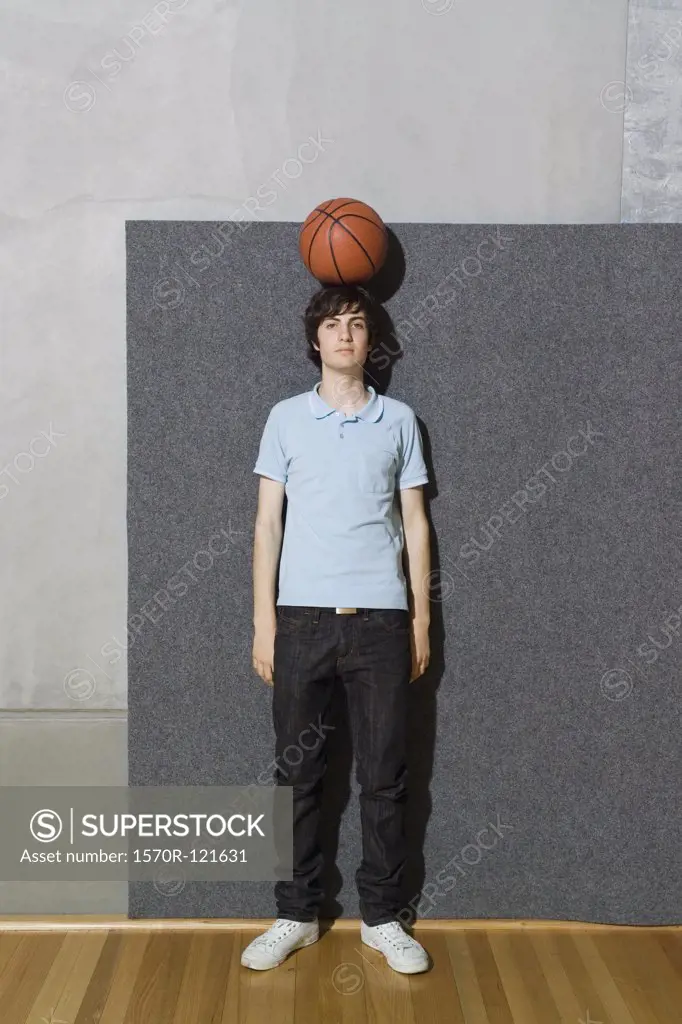 A young man standing with a basketball balanced on his head