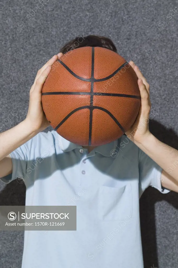 A man holding a basketball in front of his face