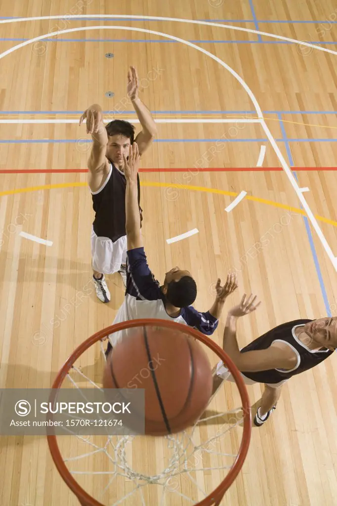 A basketball player shooting a basket and two more players playing defense