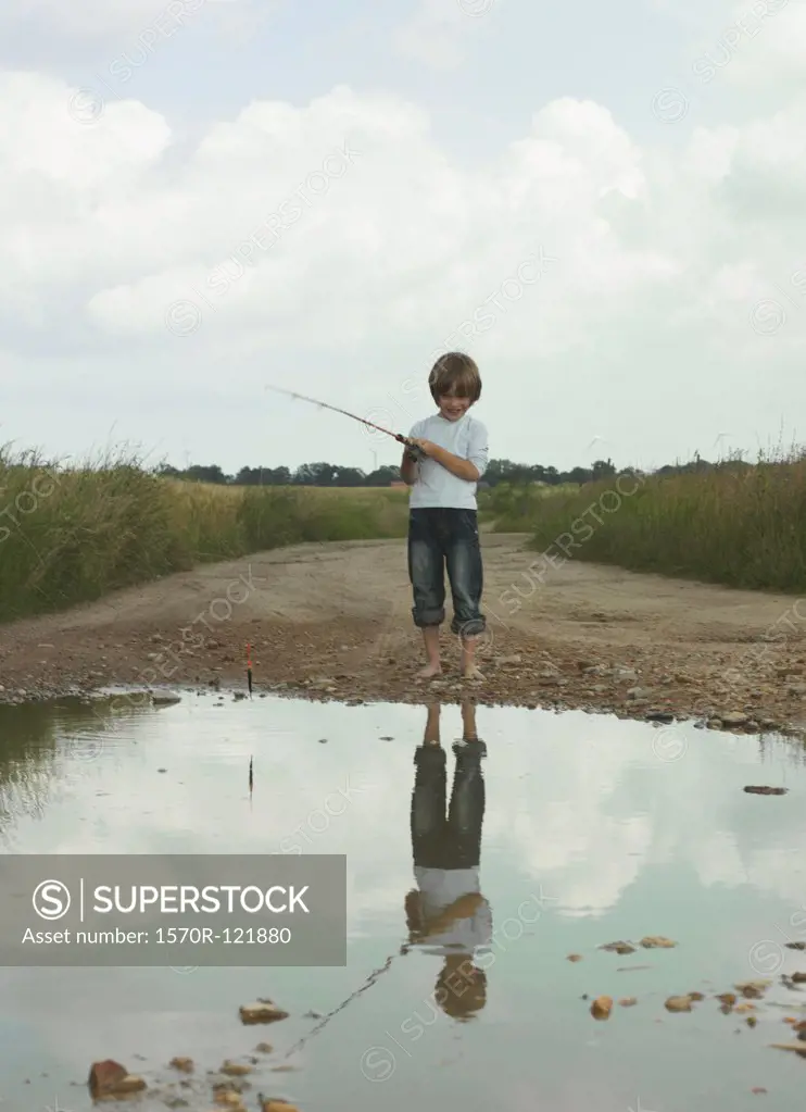 A boy fishing in a puddle