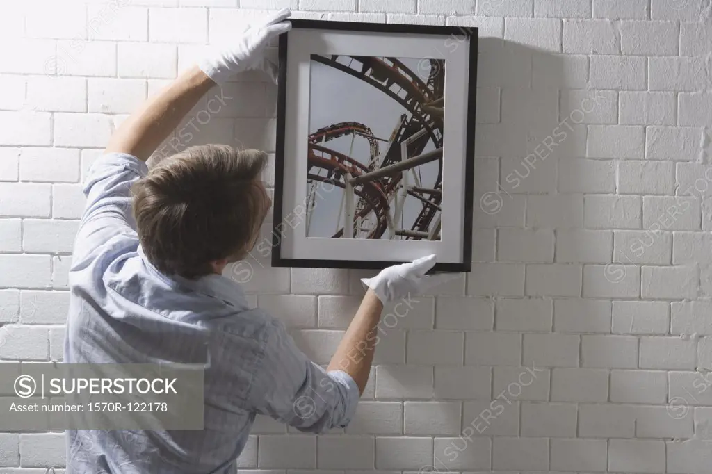 A man hanging a framed photograph on a wall