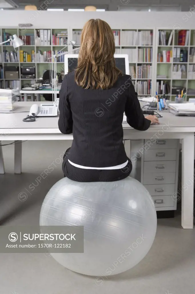 A woman sitting on an exercise ball at a desk in an office