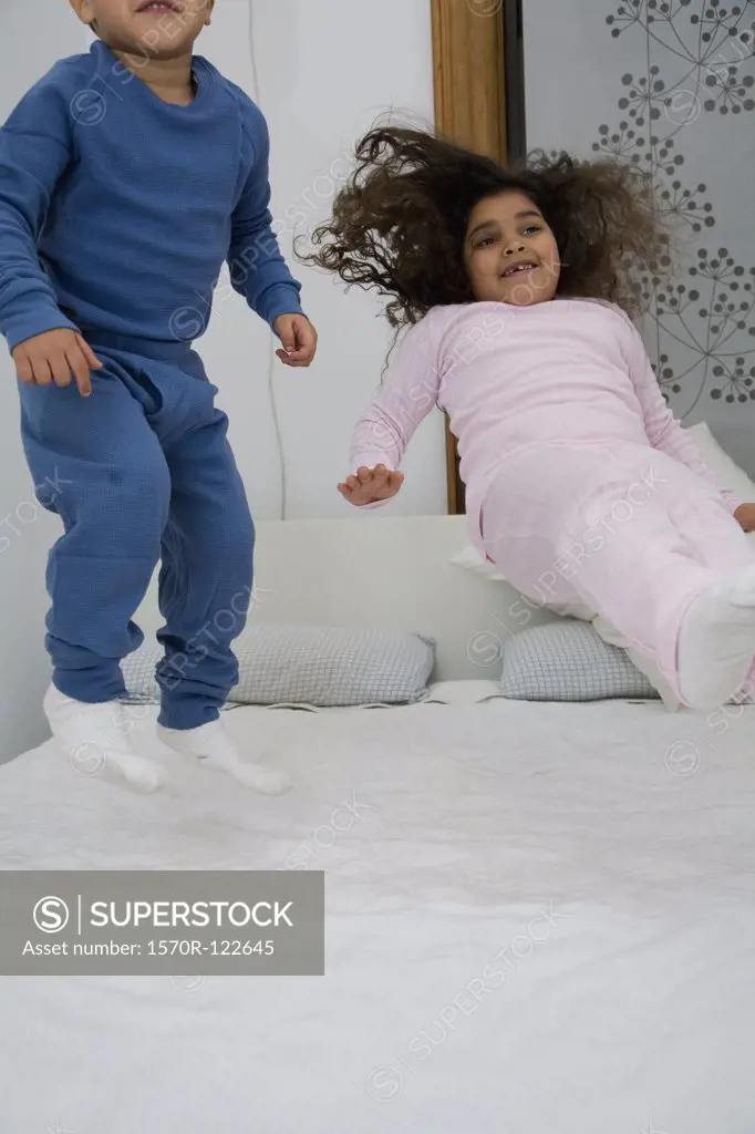 Two children jumping on a bed