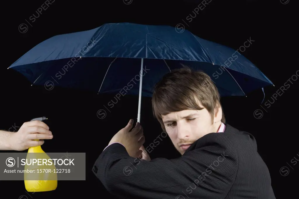 A man being squirted from a water bottle and holding an umbrella