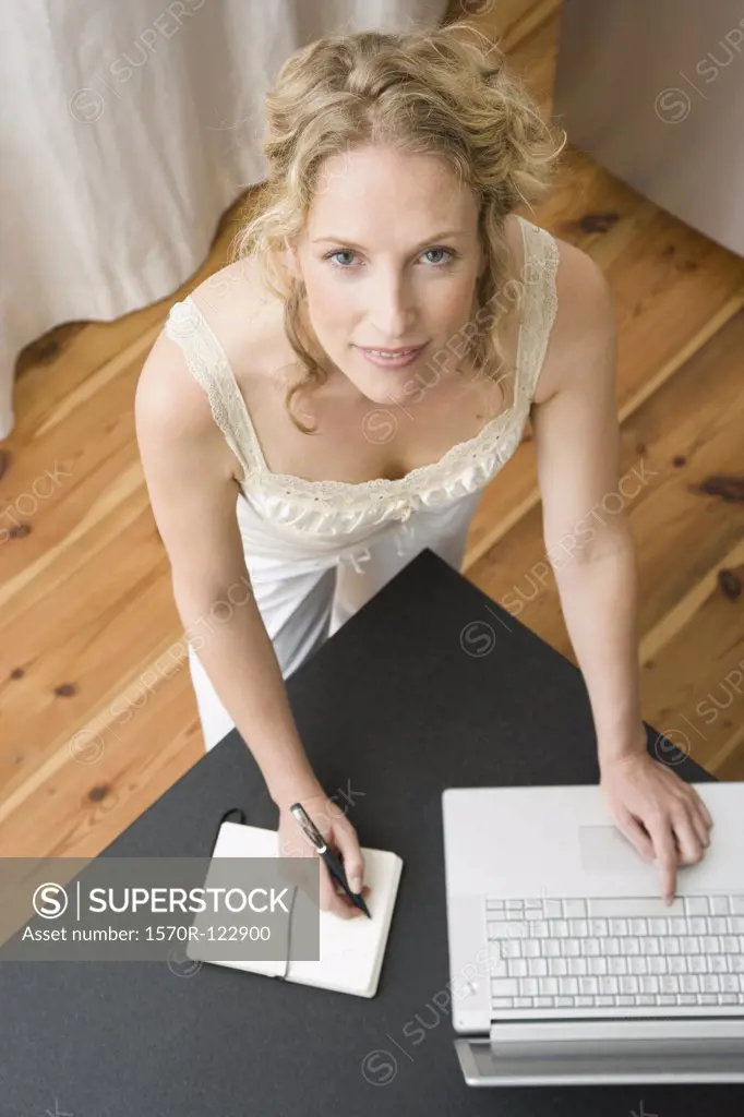 A woman writing in a notebook and using a laptop