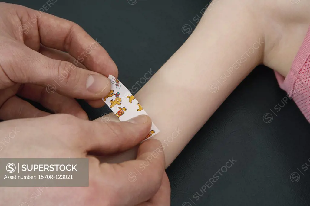 Human hands putting an adhesive bandage on a child's arm