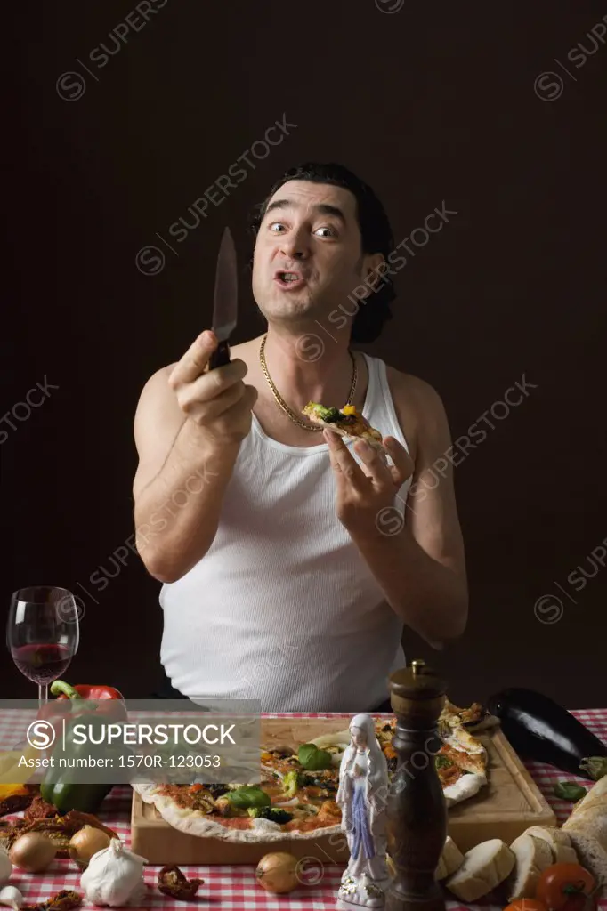 Stereotypical Italian man eating pizza and holding a knife agressively