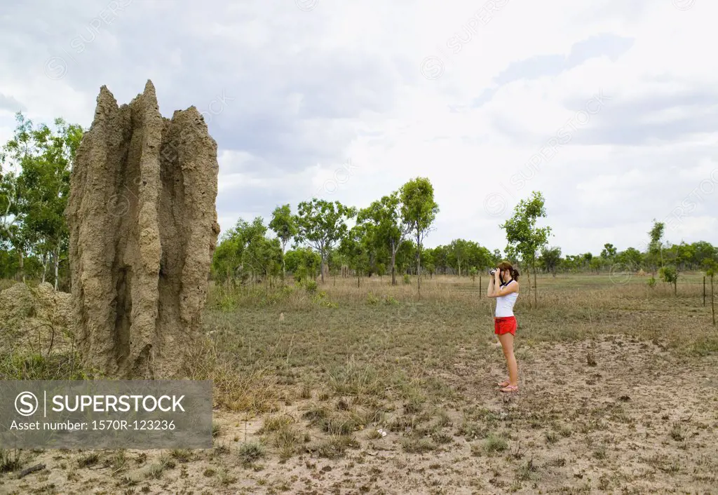 A woman taking a photograph of a termite mound