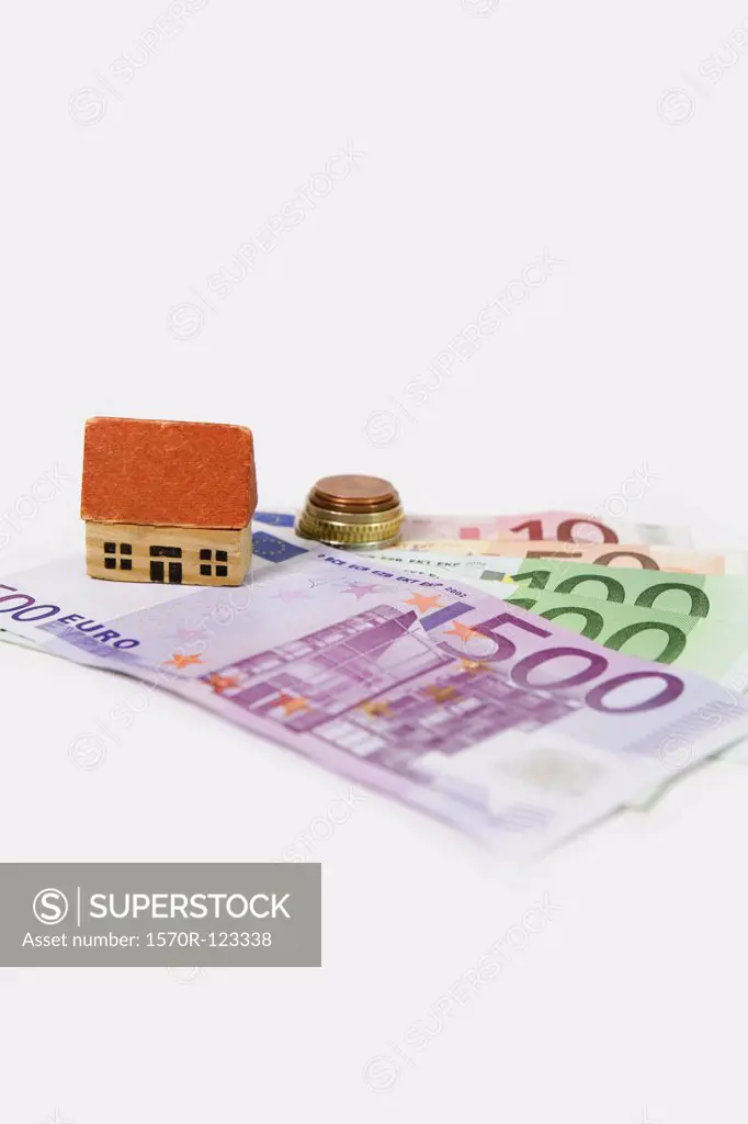 A miniature wooden house standing atop European banknotes
