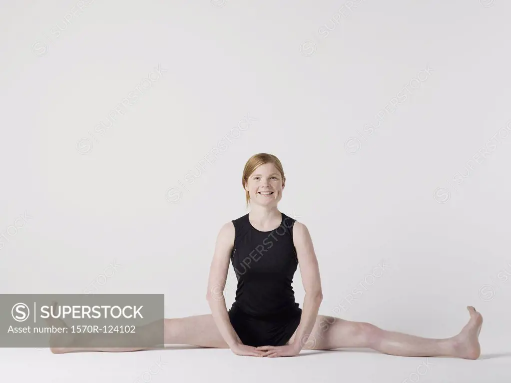 A young woman beginning the 'Spread Leg Forward Fold' yoga pose