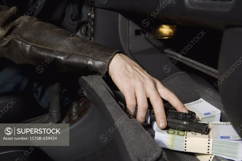A man's hand grabbing a gun from a glove compartment full of European Union currency