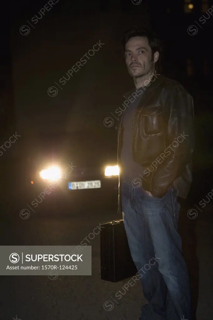 A man standing in front of headlights with a briefcase