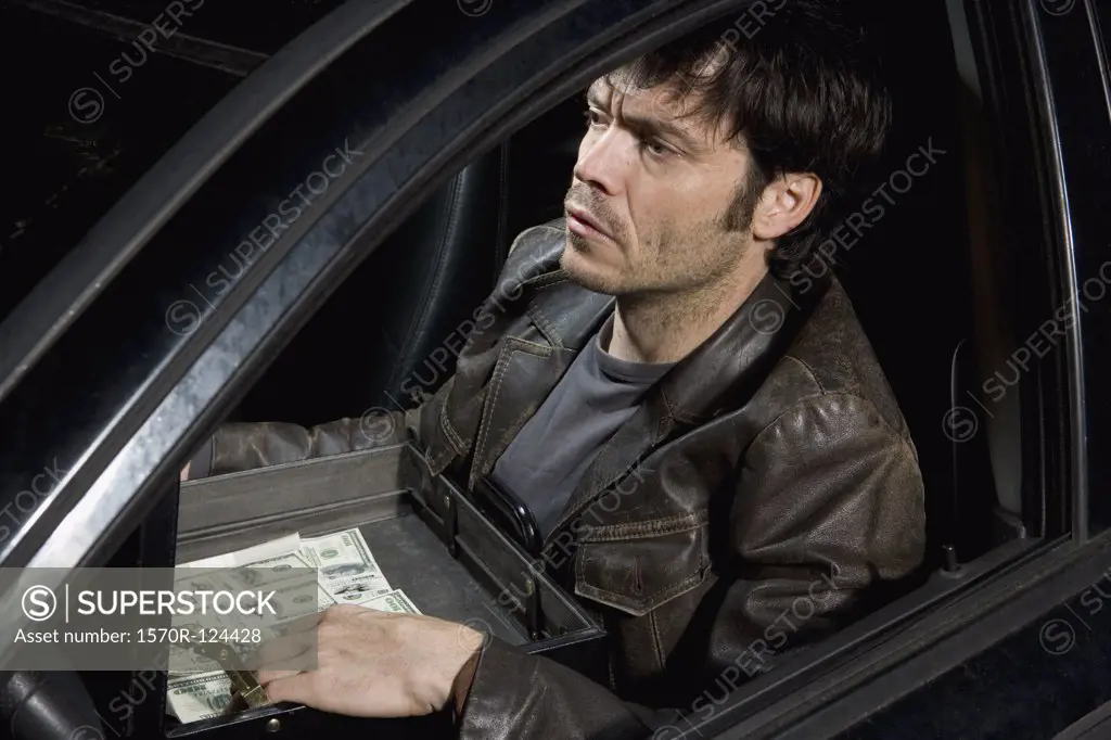 A man sitting in a car with an open briefcase full of money