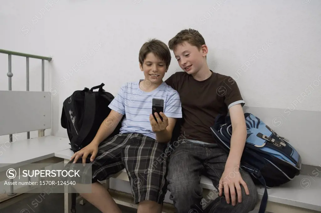 Two pre-adolescent boys sitting on a bench looking at a mobile phone