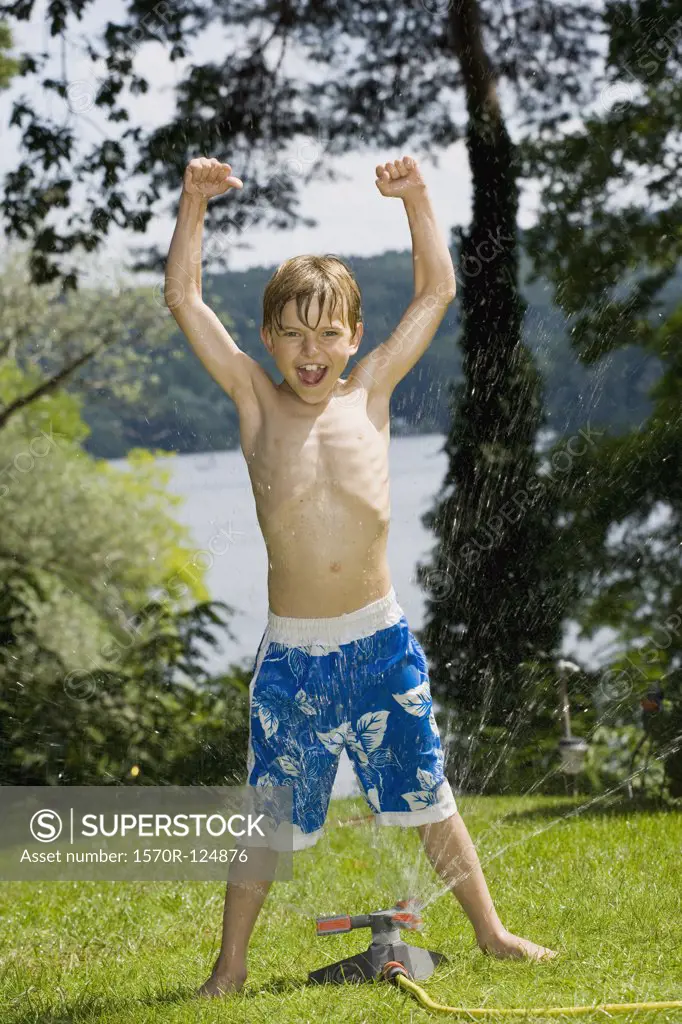 A young boy standing in a sprinkler