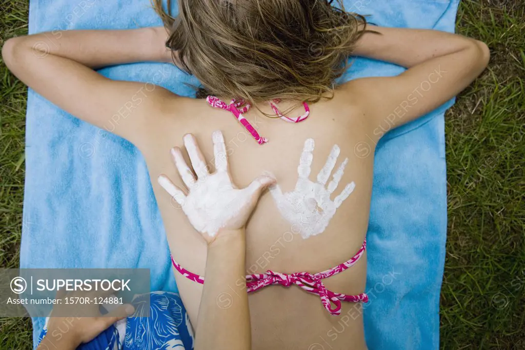 A girl with a suntan lotion handprint on her back and a boy's hand next to it