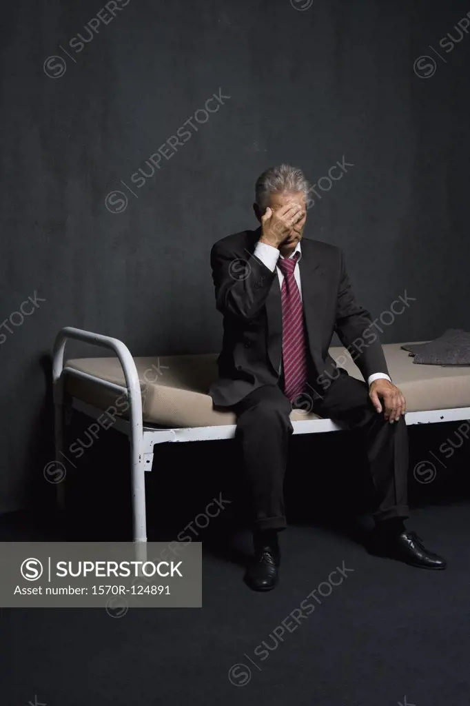 A business man sitting on a bed in a prison cell