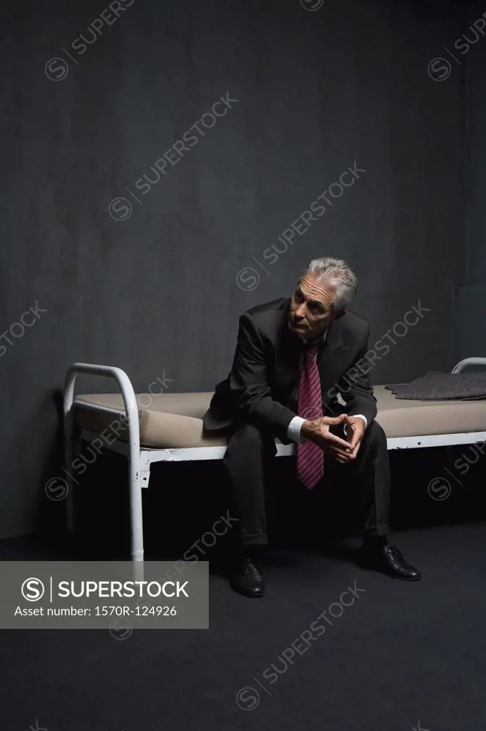 A business man sitting on a prison cell bed