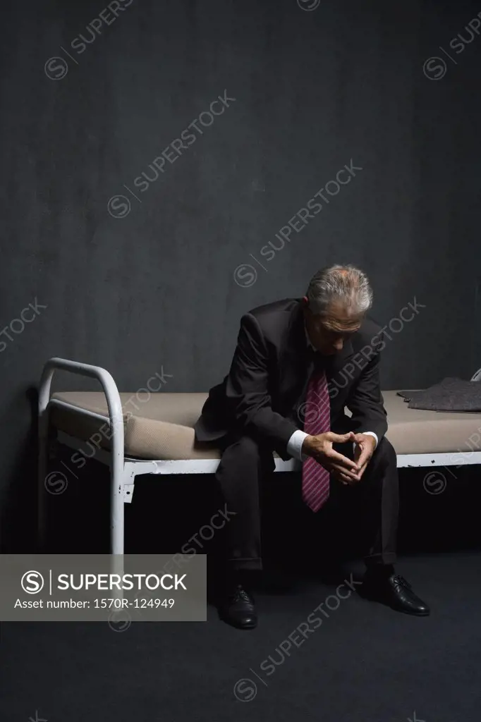 A business man sitting on a prison cell bed
