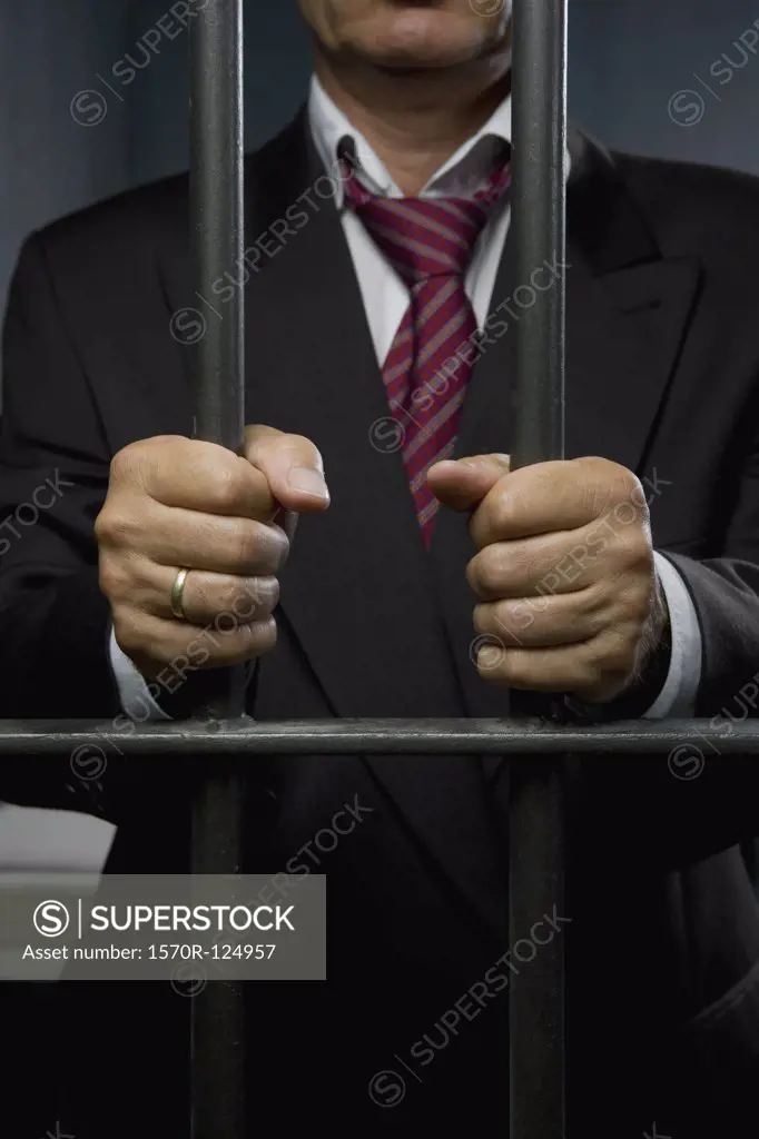 A business man standing behind prison cell bars
