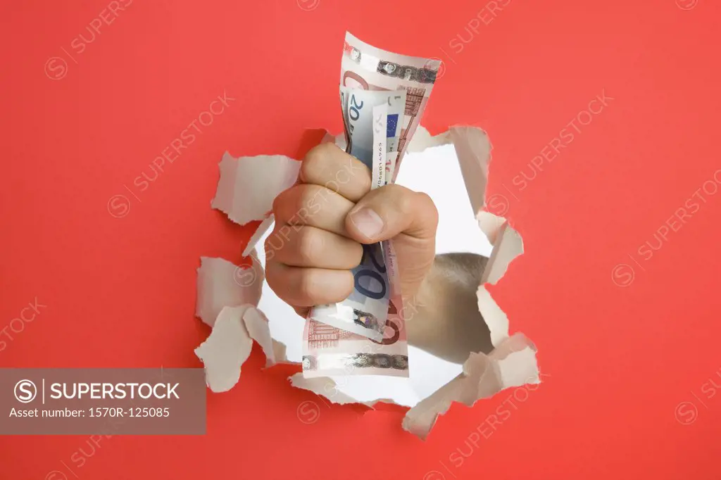 A fist breaking through a wall holding Euro banknotes