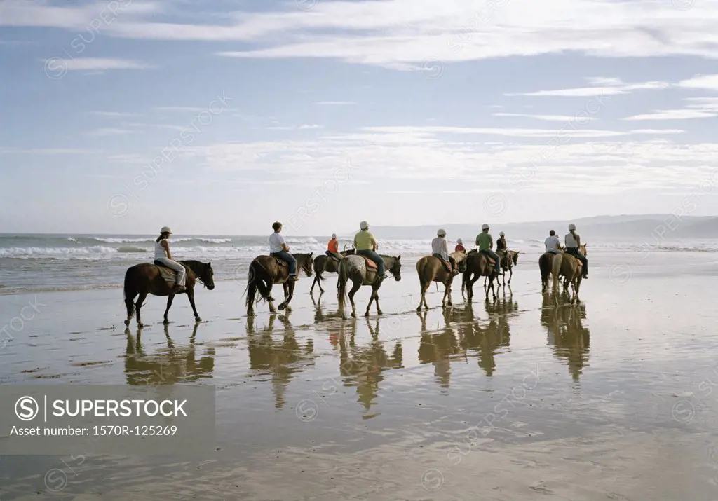 A group of people horseback riding on a beach