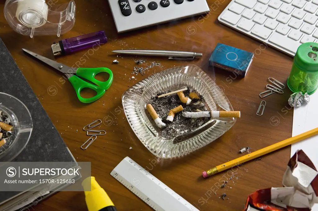 An office desk cluttered with office supplies and ashtrays