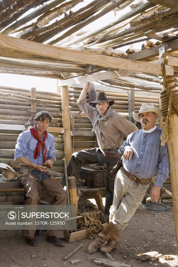 Three cowboys standing inside a wooden shed
