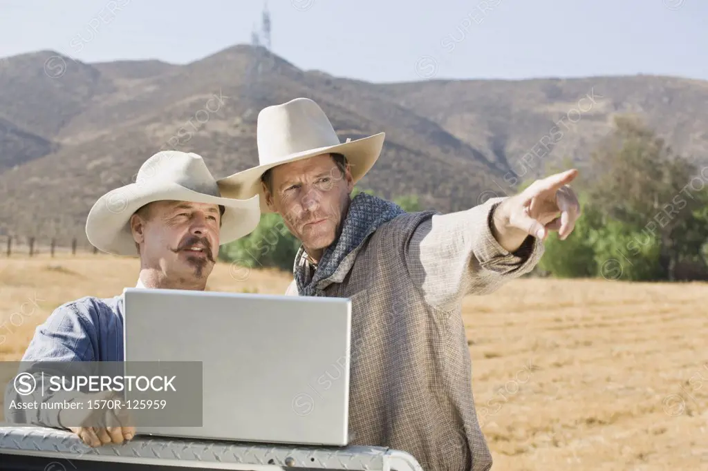 Two cowboys using a laptop and pointing