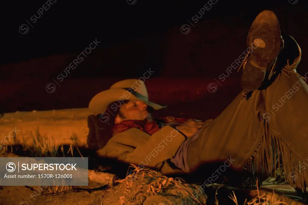 A cowboy illuminated by a campfire while sleeping