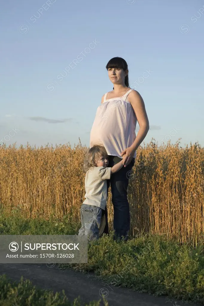 A pregnant woman and her young boy standing near a wheat field