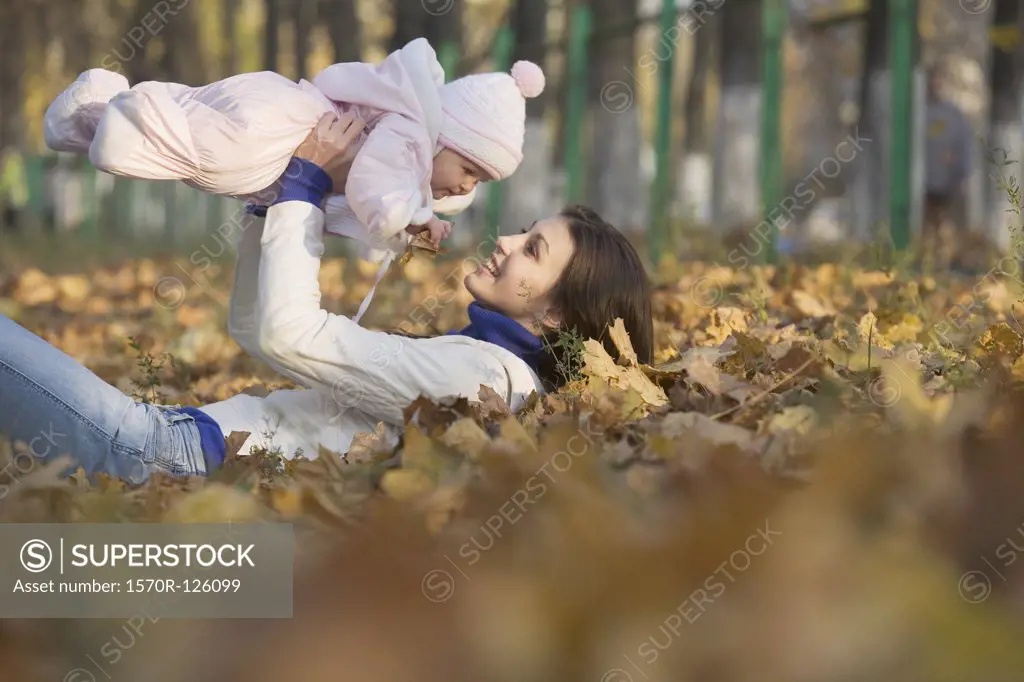 A teenage girl lying down lifting a baby up