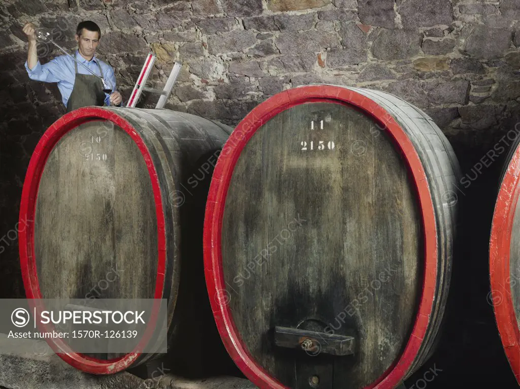 A vintner tests red wine from a barrel