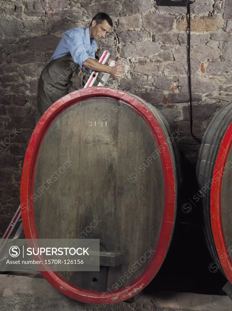 A vintner using a glass wine thief to get a sample from a barrel