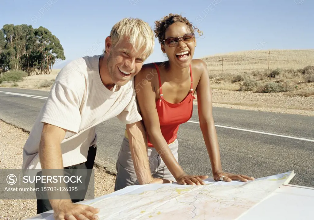 A man and a woman leaning on a car bonnet and reading a map