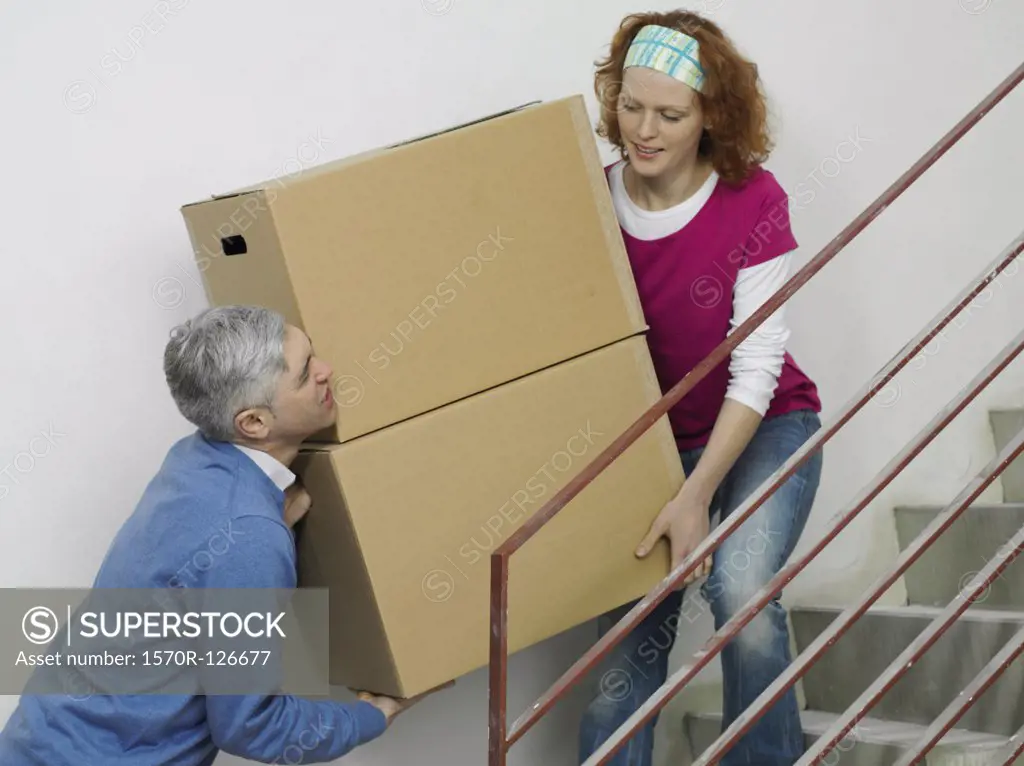 A couple carrying boxes together up stairs