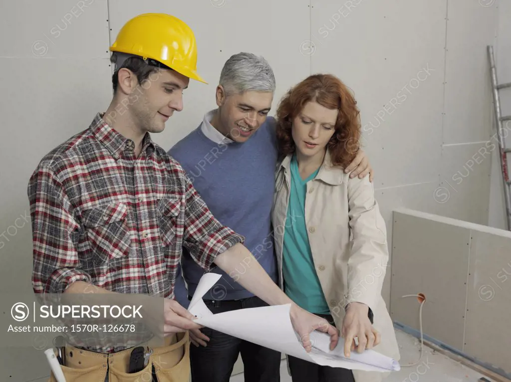 A building contractor going over blueprints with a young couple