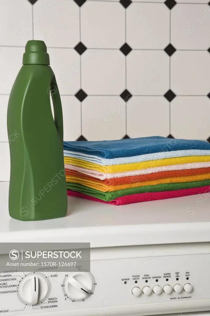 A pile of towels and a bottle of detergent on top of a washing machine