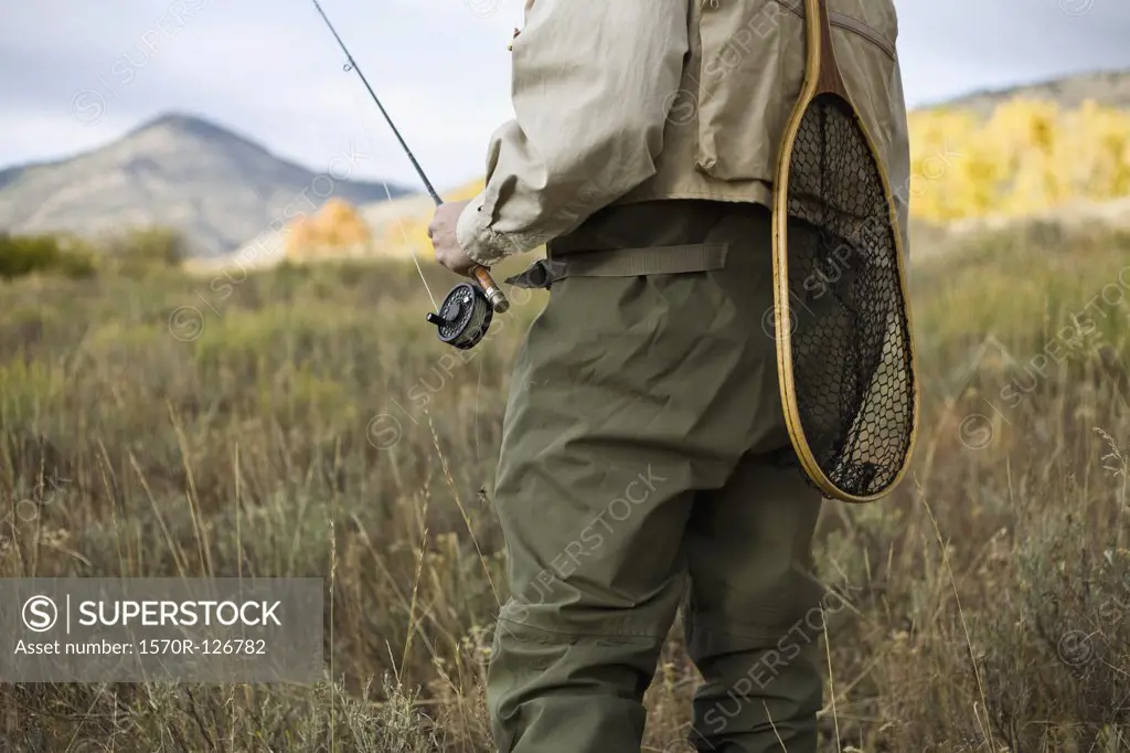Midsection of a man holding a fly rod and a fishing net