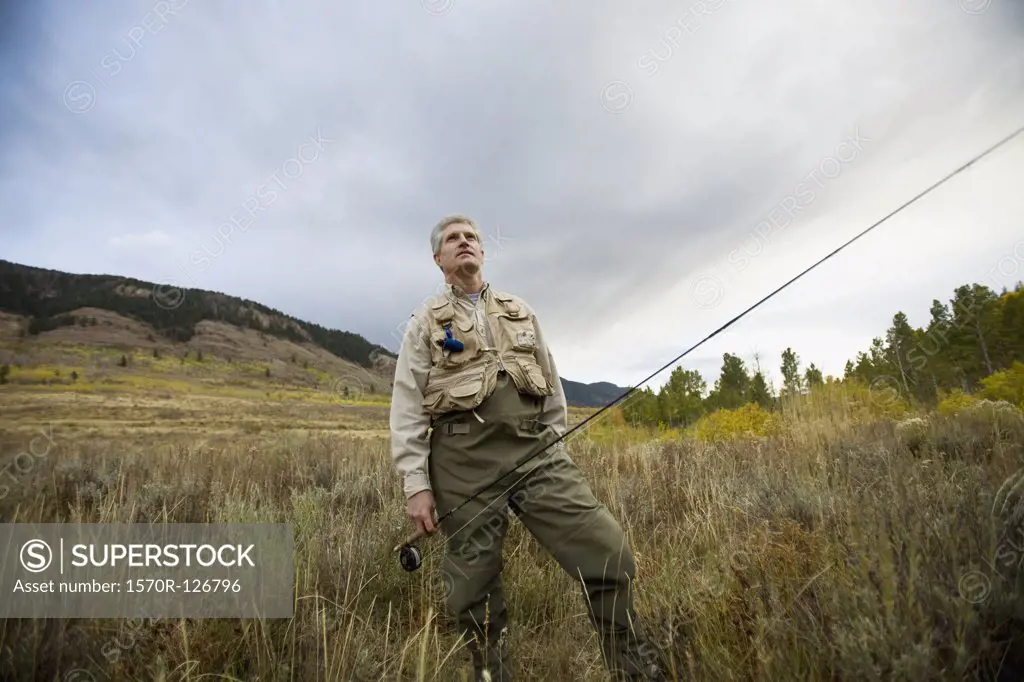 A man standing in a field with a fly rod 